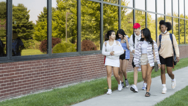 Five students walking outside of building on campus